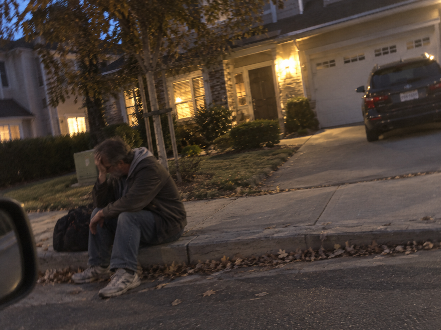 Illustrative dramatization of a man sitting alone and overwhelmed outside a home.